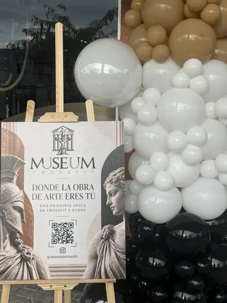 Arco de globos blancos, beige y negros junto al cartel de un evento de Museum CrossFit