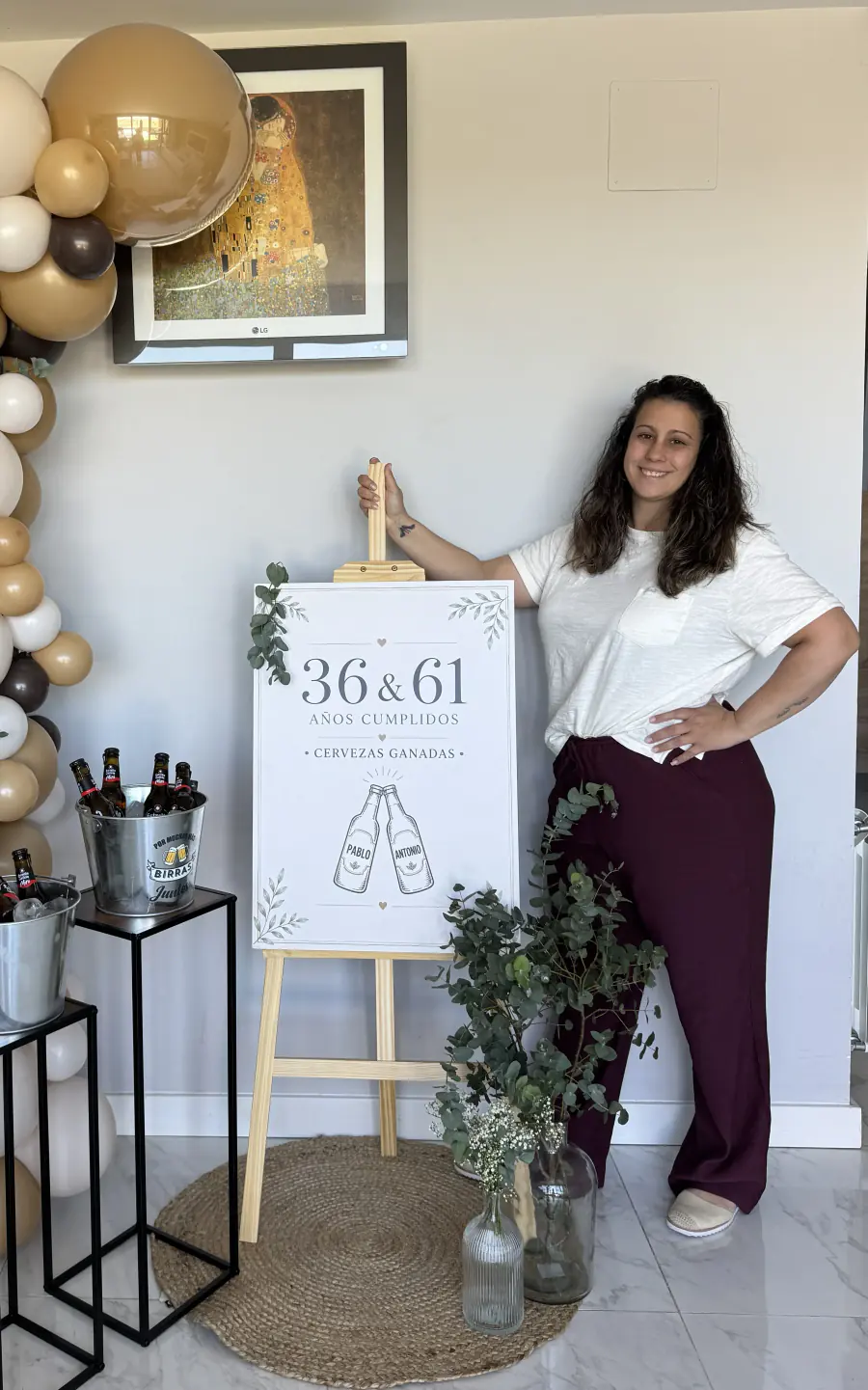 Fundadora de Azalea Atelier junto a un cartel de cumpleaños, una guirnalda de globos beige y un cubo con cervezas
