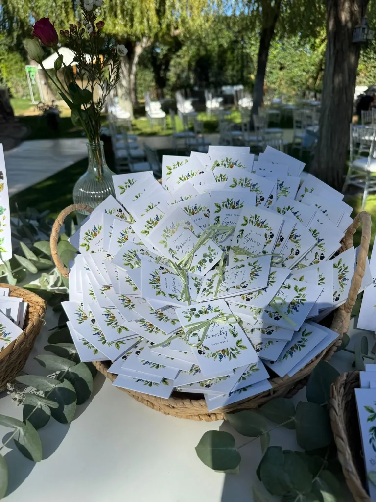 Cesta con tarjetas de boda decoradas con hojas verdes en la mesa de un jardín